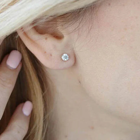 Close-up of an ear wearing a diamond stud earring with a hand holding the hair.