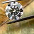 Round diamond held by tweezers on a leafy background