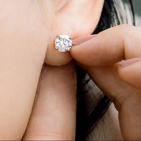 Close-up of a diamond earring being worn, with a hand adjusting it.