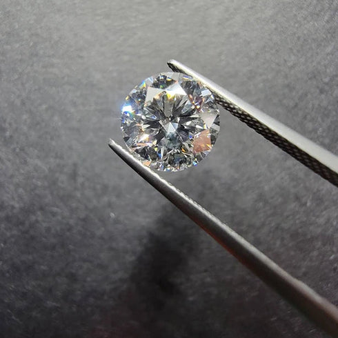 Round diamond held by tweezers against a dark background